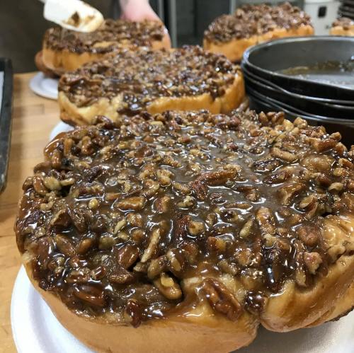 Close-up of a large, glazed donut topped with a crunchy pecan and caramel mixture.