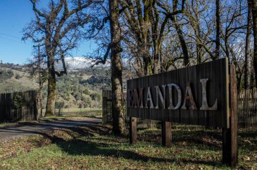 A wooden sign reading "MANDAL" at the entrance of a tree-lined road, with mountains in the background.