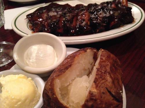 A plate of barbecue ribs with a rich sauce, served alongside a baked potato and butter.