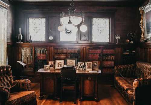 A vintage study with a wooden table, leather chairs, bookshelves, and framed photos, illuminated by stained glass windows.