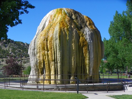 A large, colorful mineral formation resembling a dome, surrounded by trees and a railing in a park setting.