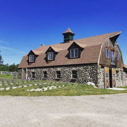 A rustic stone building with a peaked roof and a cupola, surrounded by green grass and a clear blue sky.