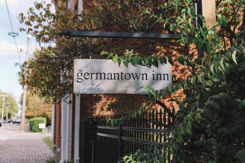 Sign for "The Germantown Inn" surrounded by greenery, with a brick building in the background.