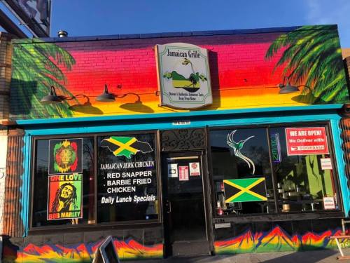 Colorful Jamaican Grille exterior with vibrant murals, featuring palm trees, a parrot, and a sign for daily lunch specials.