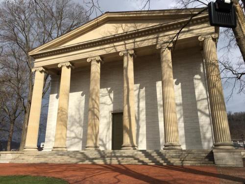 A classical-style building with tall columns and a pediment, surrounded by trees and a pathway.