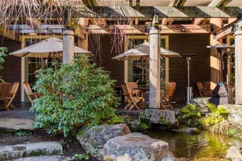 A serene outdoor seating area with wooden chairs, umbrellas, and a small pond surrounded by greenery.