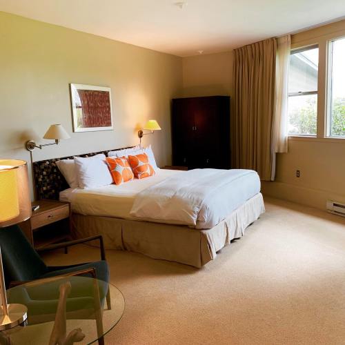 Cozy bedroom with a bed, armchair, and large windows, featuring warm colors and soft lighting.