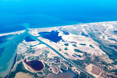 Aerial view of coastal land with water bodies, sandy areas, and a blue ocean in the background.