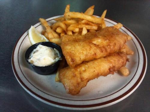 A plate of golden fried fish fillets with French fries and a side of tartar sauce and a lemon wedge.