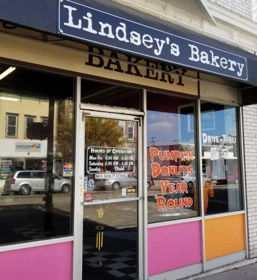 Exterior of Lindsey's Bakery featuring a colorful storefront and a sign advertising pumpkin donuts year-round.