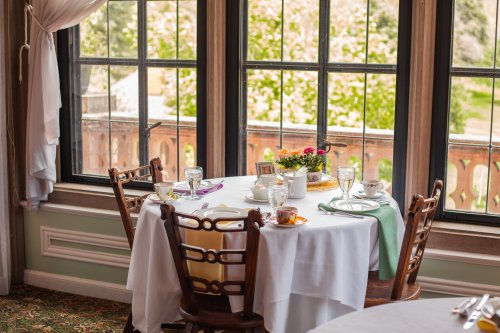 A beautifully set dining table by a window, featuring dishes, glasses, and a small flower arrangement.