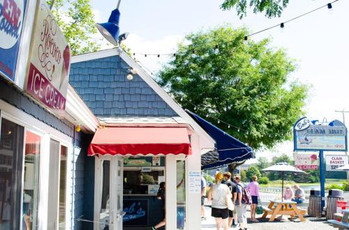 A charming seaside scene featuring ice cream shops, people walking, and trees with string lights overhead.