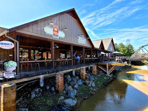 A rustic restaurant by a river, featuring outdoor seating and signs for Hershey's Ice Cream and Taco Bell.