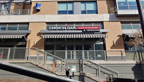 Exterior of Smokin' Oak, a wood-fired pizza and taproom, featuring a sign and awnings on a brick building.