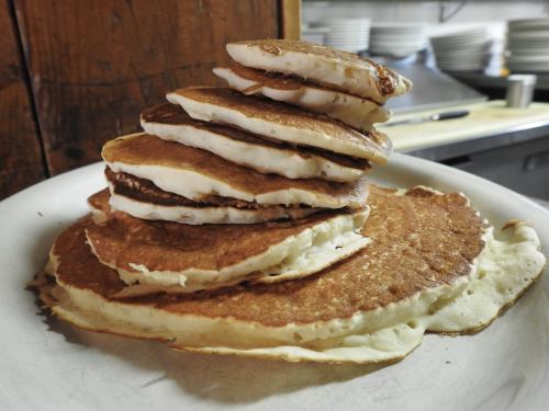 A stack of golden-brown pancakes on a white plate, with a rustic kitchen background.