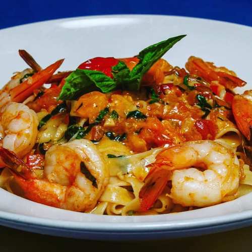 A plate of pasta topped with shrimp, herbs, and a rich tomato sauce, garnished with fresh basil.