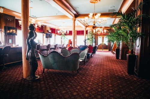 Elegant interior of a lounge with plush seating, decorative plants, and chandeliers, featuring a vintage sculpture.