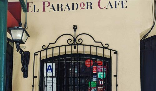 A cozy café entrance with a decorative window, two cocktails on a table, and vibrant seating.