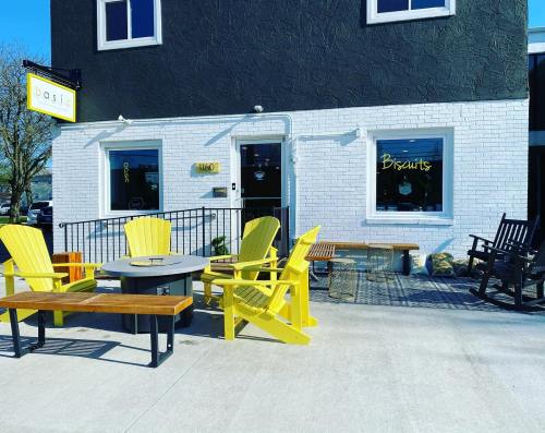 A cozy outdoor seating area with yellow chairs and a table in front of a modern building with a sign for "Biscuits."