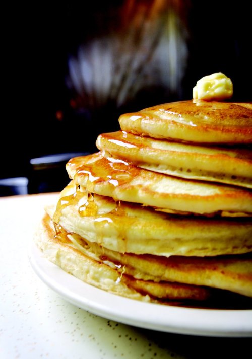 A stack of fluffy pancakes drizzled with syrup and topped with a pat of butter on a white plate.