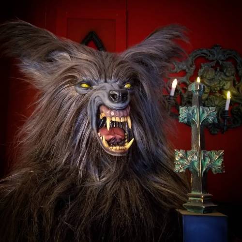 A fierce, snarling wolf-like creature with glowing eyes, set against a red background and a decorative cross with candles.