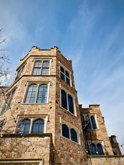 A tall stone building with large windows under a clear blue sky, showcasing architectural details and a staircase.