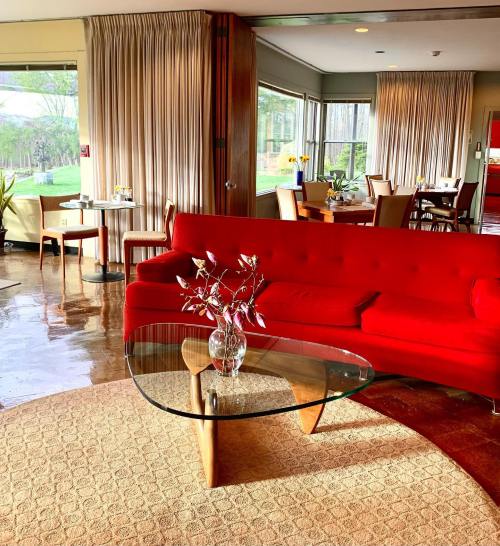 A cozy living room featuring a red sofa, glass coffee table, and warm lighting, with a view of greenery outside.