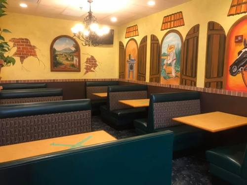 Cozy restaurant interior with green booths, wooden tables, and colorful mural depicting scenic views.