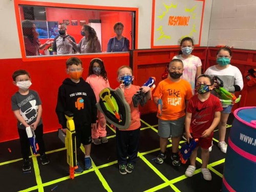 A group of children wearing masks, holding toy guns, in a colorful indoor play area with a "RESPAWN" sign.
