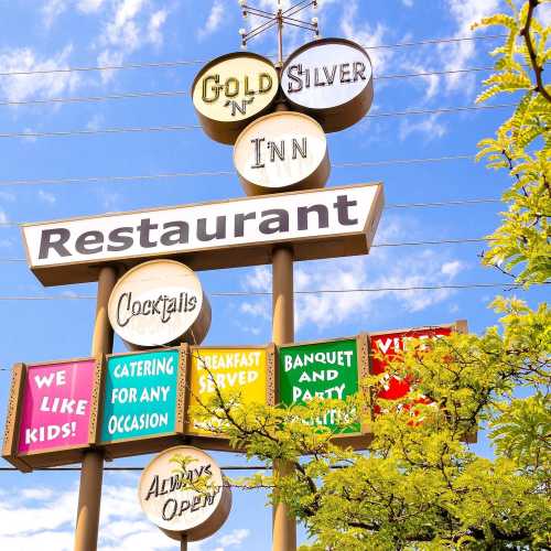 Sign for Gold 'n' Silver Inn Restaurant featuring various offerings like breakfast, catering, and banquets, surrounded by greenery.