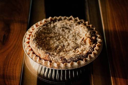 A freshly baked pie in a silver tin, resting on a wooden surface, with a golden-brown crust and crumbly topping.