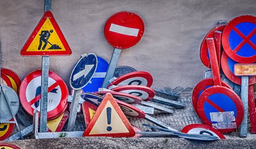 A chaotic arrangement of various traffic signs, including warning, prohibition, and directional signs, leaning against a wall.