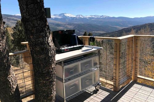 A grill on a wooden deck with a stunning mountain view in the background, surrounded by trees.