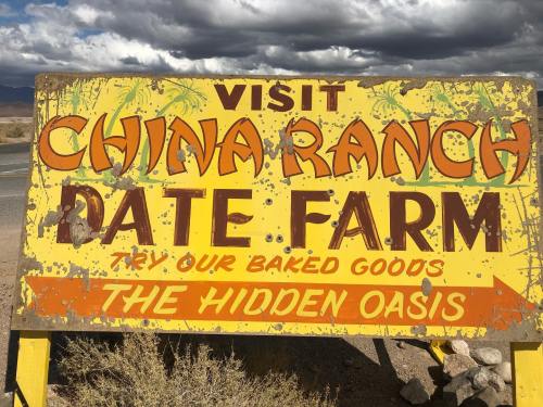 Sign for China Ranch Date Farm, promoting baked goods and describing it as "The Hidden Oasis." Desert landscape in background.
