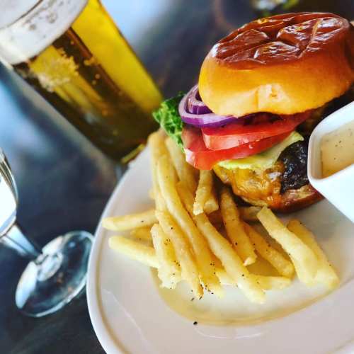A juicy burger with lettuce, tomato, and onion, served with crispy fries and a glass of beer in the background.