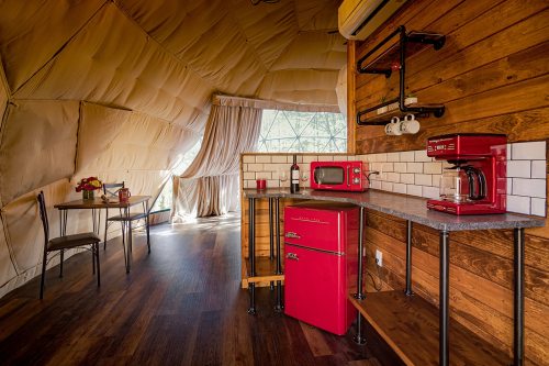 Cozy kitchen in a geodesic dome, featuring red appliances, wooden accents, and a small dining table.