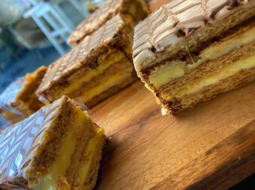 Close-up of layered dessert with creamy filling and chocolate topping, arranged on a wooden surface.