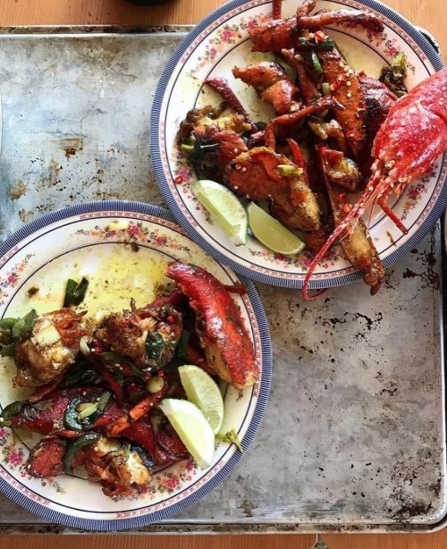 Two plates of seafood featuring lobster and crab, garnished with lime and herbs, on a metal tray.