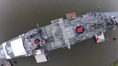 Aerial view of a large naval ship docked in water, showcasing its deck and equipment.