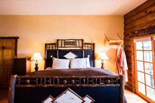 Cozy bedroom with a wooden bed, two lamps, and a log cabin wall, featuring a robe hanging by the door.