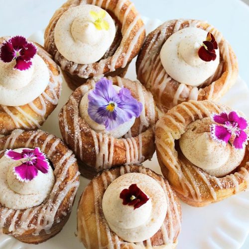 A plate of beautifully decorated cinnamon rolls topped with cream and edible flowers.