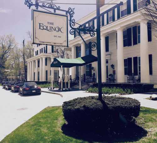 A historic building with a sign reading "The Equinox," surrounded by greenery and parked cars.