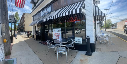 A restaurant exterior with striped awnings, outdoor seating, and a "Take Out Available" sign.