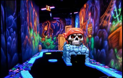 A vibrant mini-golf course featuring a pirate theme, with a large skull and colorful glowing decorations.