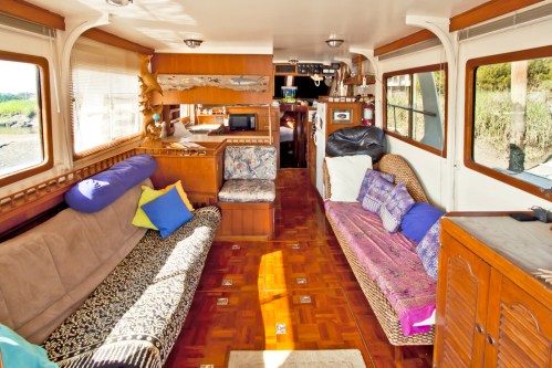 Cozy interior of a boat featuring comfortable seating, colorful cushions, and wooden decor, with natural light streaming in.