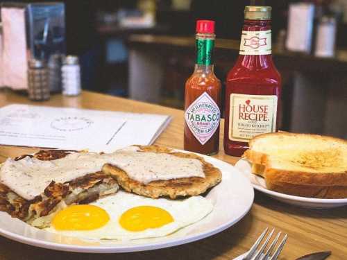 A plate of breakfast featuring two eggs, hash browns, sausage gravy, toast, and bottles of Tabasco and ketchup.