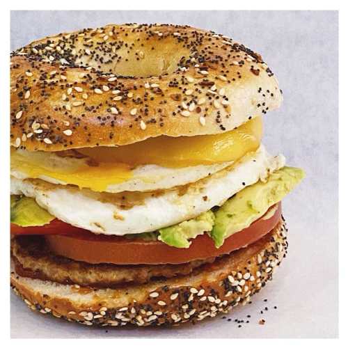 A toasted bagel sandwich with egg, cheese, avocado, and tomato, topped with poppy and sesame seeds.