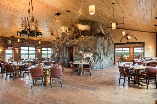 Rustic restaurant interior with wooden decor, animal mounts, and tables set for dining. Large stone feature in the center.