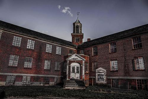 Abandoned brick building with a clock tower, featuring broken windows and a weathered entrance.