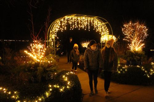 Two children walk under a lit archway, surrounded by glowing decorations and trees at night.